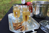 Three glass mugs of cider with the Orange Clove Hot Toddy Kit, cinnamon sticks, and whiskey spices on a tray.