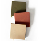 Three Square Linen Journals in green, red, and beige are arranged diagonally on a white background.