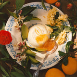 A dessert topped with Ruby Valencia Orange and Apricot Marmalade, served on a plate with flowers, leaves, and oranges.