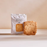 A Salted Caramel Single Shortbread Cookie sits unwrapped by its Rustic Bakery box on a beige surface.