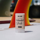 SIN-MIN Shade sunscreen stick on a white surface with blurred background