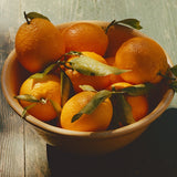 A bowl of oranges with green leaves on rustic wood—ideal for Ruby Valencia Orange and Apricot Marmalade.