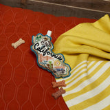 A California Dog Toy, dog treats, and a patch on a yellow-striped blanket over an orange quilted surface.