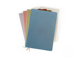 Four pastel Linen Hardcover Journals are stacked on white, with the blue one on top.