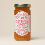 A jar of Ruby Valencia Orange and Apricot Marmalade with a gold lid and a pink-and-white label.