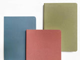 Three Linen Hardcover Journals in blue, red, and green are arranged on a white surface.