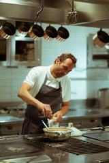 A chef in an apron cracks an egg, ready to drizzle Shiitake Mushroom Oil in a professional kitchen.