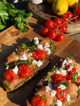 Two slices of toast with Zhough Dip & Spread, tomatoes, smoked salmon, cheese, herbs, lemon, and parsley.