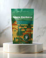 A 5oz bag of Santa Barbara Souvenir Dog Treats with a scenic illustration, shown on a marble tray.