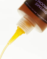 Shiitake Mushroom Oil pours from an upside-down bottle with a pointed cap against a white background.