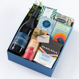 The Alma Rosa Craft Connoisseur Gift Box features a bottle of Sta Rita Hills Pinot Noir, coffee, tea, a chocolate bar, cookies, organic pistachios, and a small plant—all beautifully packaged in a blue gift box.