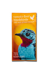 The Artisanal Chocolate Bar 1.4oz features an orange wrapper with a blue and red bird illustration, a white bird silhouette in the top right corner, and is labeled “twenty-four blackbirds HAND-MADE ARTISAN DARK CHOCOLATE, 75% Wampu Sirpi.”.