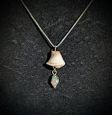 The Australian White Opal Necklace features a silver chain with a seashell mushroom pendant and an iridescent teardrop gemstone, inspired by handmade opal jewelry and set against black fabric.
