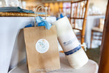 A Custom Logo Beach & Bath Towel in a gift bag on a chair at an event, with Santa Barbara logo and photo credit.