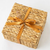 The California Farm Snacks Gift Basket is a square woven basket with a golden satin bow and dried flowers, featuring organic pistachios. Perfect for gifting, it's shown on a plain white background.