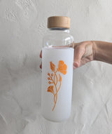 A hand holds the Custom Logo Water Bottle from the California Welcome Gift Basket, featuring a bamboo lid and orange floral design—ideal for pairing with local treats or as a thoughtful California gift.