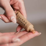 A person squeezes Churro Lip Scrub from a small brown tube onto their finger with painted nails.