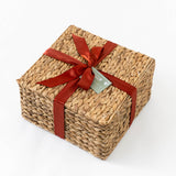 A rectangular woven basket made from recycled paper, decorated with a red satin ribbon bow and a Custom Logo Gift Tag, displayed on a white background.