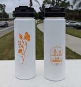 Two white Custom Logo Sequoia Stainless Tumblers with black lids sit on a ledge—one displays an orange flower, the other features a bridge and "Destinations San Francisco 2024." Trees and a street can be seen in the background.