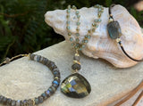Labradorite Reflection Bracelet displayed beside a large seashell with other jewelry pieces from the collection.