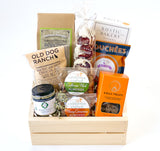 The Golden State Gift Basket is a wooden crate filled with artisan California foods like popcorn, breadsticks, cookies, hot chocolate walnuts, almonds, tapenade, and chocolate-covered treats—all beautifully arranged.
