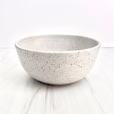 The Handmade Klapp Ceramic Planter, a simple round white bowl with black speckles by Atlas Klapp Ceramics in Santa Barbara, sits on a light marble surface against a plain white background.