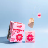 A pink box of Hibiscus Glow Tea sits beside an individual tea bag packet and a floating caffeine-free hibiscus tea bag, all displayed on a light blue background.