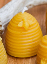 The Hive Beeswax Candle is a yellow, beehive-shaped candle with a decorative bee on its side, displayed on wood—a charming natural accent for your home.