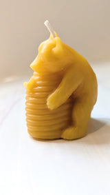 The Honey Bear Hugging Hive Beeswax Candle features a bear embracing a hive, crafted from natural yellow beeswax with a white wick—ideal for fans of unique, eco-friendly candles.