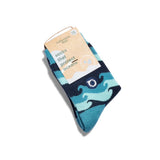 A pair of blue Kids Socks that Protect Oceans, folded with a label reading Conscious Step: socks that protect healthy oceans. They feature dark wave patterns, a small wave emblem, and support Oceana’s mission.