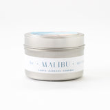 The Malibu Travel Candle from Santa Barbara Company is a 3oz soy wax candle in a small silver tin, perfect for travel. Set against a plain white background.