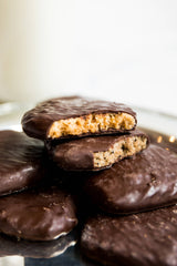 A close-up of Milk Chocolate Caramelized Graham Crackers stacked on a plate, with the top cracker broken in half to reveal a golden, crumbly interior made from organic ingredients.