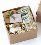 The Montecito Classic Petite Gift Box includes a gold-tinned Montecito candle, assorted truffles with a green ribbon, and organic salted pistachios, all nestled in shredded paper filler.