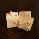Three Ojai Pixie Handcrafted Soaps, with cream and pink marbled swirls and dried flower petals on top, are stacked on dark wood. Infused with natural essential oils, their citrus scent adds a refreshing, artisanal touch.