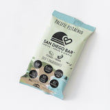 The San Diego Bar Pacific Pistachio Snack Bar comes in a light green and blue wrapper, is vegan, raw, plant-based, gluten-free, all natural, and packs 10g protein—a tasty gluten-free snack for healthy living.