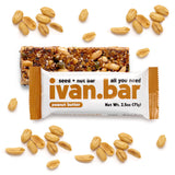 A Peanut Butter Ivan Bar lies unwrapped on a white background, surrounded by roasted peanuts. The open bar displays a tempting blend of superfood seeds and nuts.