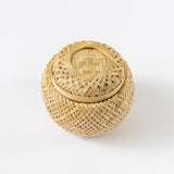 The Petite Tea Gift Basket is a round, lidded basket made from light-colored woven bamboo. Its intricate design adds decorative texture, making it ideal for gifting items like a Honey Sampler or Olive Leaf Tea Bags.