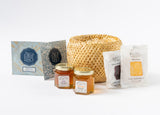 The Petite Tea Gift Basket features a honey sampler, two Rustic Bakery shortbread cookies, and Steep Echo Olive Leaf Tea Bags, all beautifully arranged in a wicker basket on a white surface.