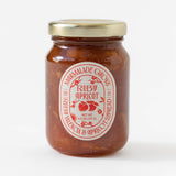 A glass jar with a gold lid holds Ruby Valencia Orange and Apricot Marmalade. The white label features red text and apricot illustrations, stating handmade marmalade with Valencia oranges & apricots, 4.5 oz (127g).