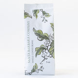 A white 5 oz SBCO Coffee bag labeled Whole Coffee Beans, featuring green leaves and coffee beans illustrations on the front—ideal for savoring delicious, organic coffee.