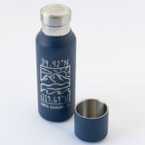 The Santa Barbara Coordinates Insulated Bottle & Cup Set includes a navy blue stainless steel bottle with copper vacuum insulation, a silver cap, white line art of mountains and ocean, coordinates, "Santa Barbara, CA," and optional logo.