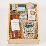 The Santa Barbara Rosé Gift Box includes a bottle of Rosé, a candle, cookies, a matchbox, a small painting, a wooden coaster, and organic pistachios in crinkle paper—a California gourmet gift for any occasion.