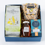 The Santa Barbara Simplicity Gift Box includes sea salt & olive oil organic popcorn, lemon salt pistachios, wildflower honey, and Steep Echo Ascent herbal tea, all attractively arranged on brown crinkle paper.