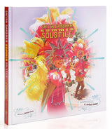 The cover of the coffee table book "Santa Barbara Summer Solstice" shows people in vibrant feathered costumes, with someone in a pink and yellow headdress smiling at the center. The title appears in bold, festive letters.