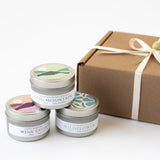The Santa Ynez Valley Candle Trio Gift Set features small plant-based soy candles—Fig Mountain, Wine Country, and Wildflower—stacked by a brown gift box with a cream ribbon and dried flower, capturing Santa Barbara's minimalistic charm.