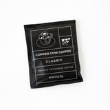 A Single-Serve Pour Over Classic Black Coffee packet by Copper Cow Coffee, featuring white line art of a cup and phin filter, displays net weight 0.42 oz (12g) on a white background.