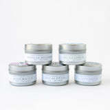 Five small silver tins from the Travel Candle Gift Set are stacked in a pyramid. Labels display scents: Vanilla Bourbon, Wildflower, Rosewater, Eucalyptus, and Lavender. Ideal as a natural candle gift, set against a plain white background.