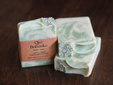 Two bars of White Sage Ojai Botanika Soap with green and white swirls, topped with dried sage leaves, are displayed on a dark wooden surface—handcrafted vegan soap made with pure essential oils and always cruelty-free.