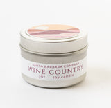 The Wine Country Travel Candle is a small silver tin from Santa Barbara Company with a soy wax fill and a decorative lid showcasing a warm, minimalist sunset design—ideal as a travel-friendly candle for any getaway.
