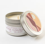 The Wine Country Travel Candle is a small metal tin with a soy wax candle inside. The lid shows an abstract mountain landscape, making it the perfect travel-friendly candle for wine country adventures from Santa Barbara Company.